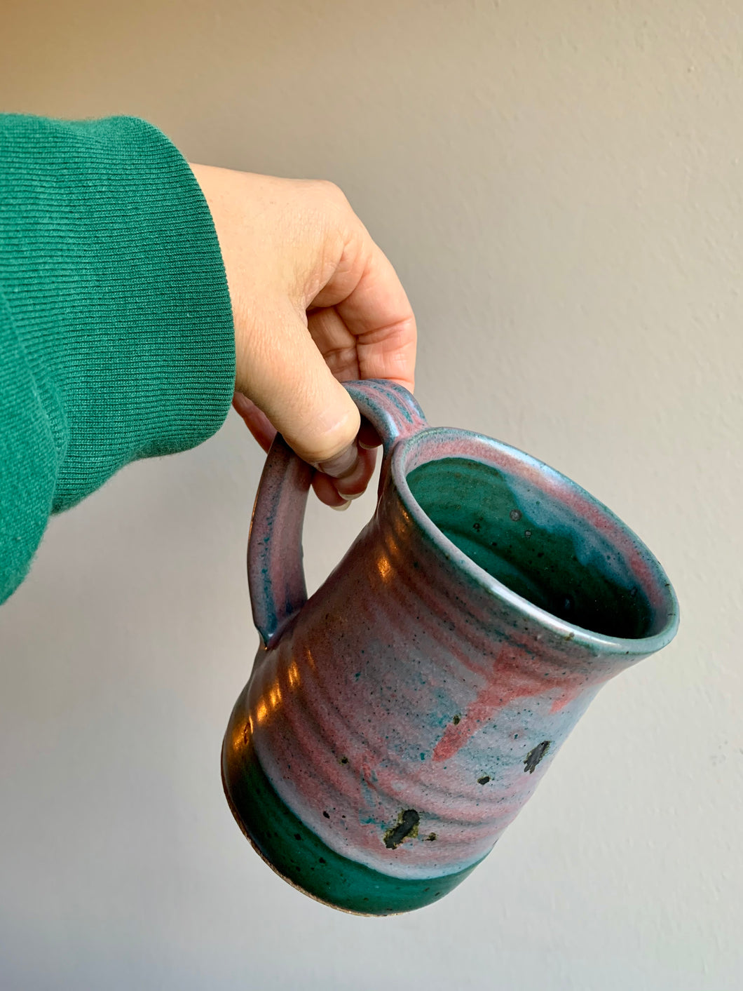 Woman holds a dark green and pink glazed pottery mug.